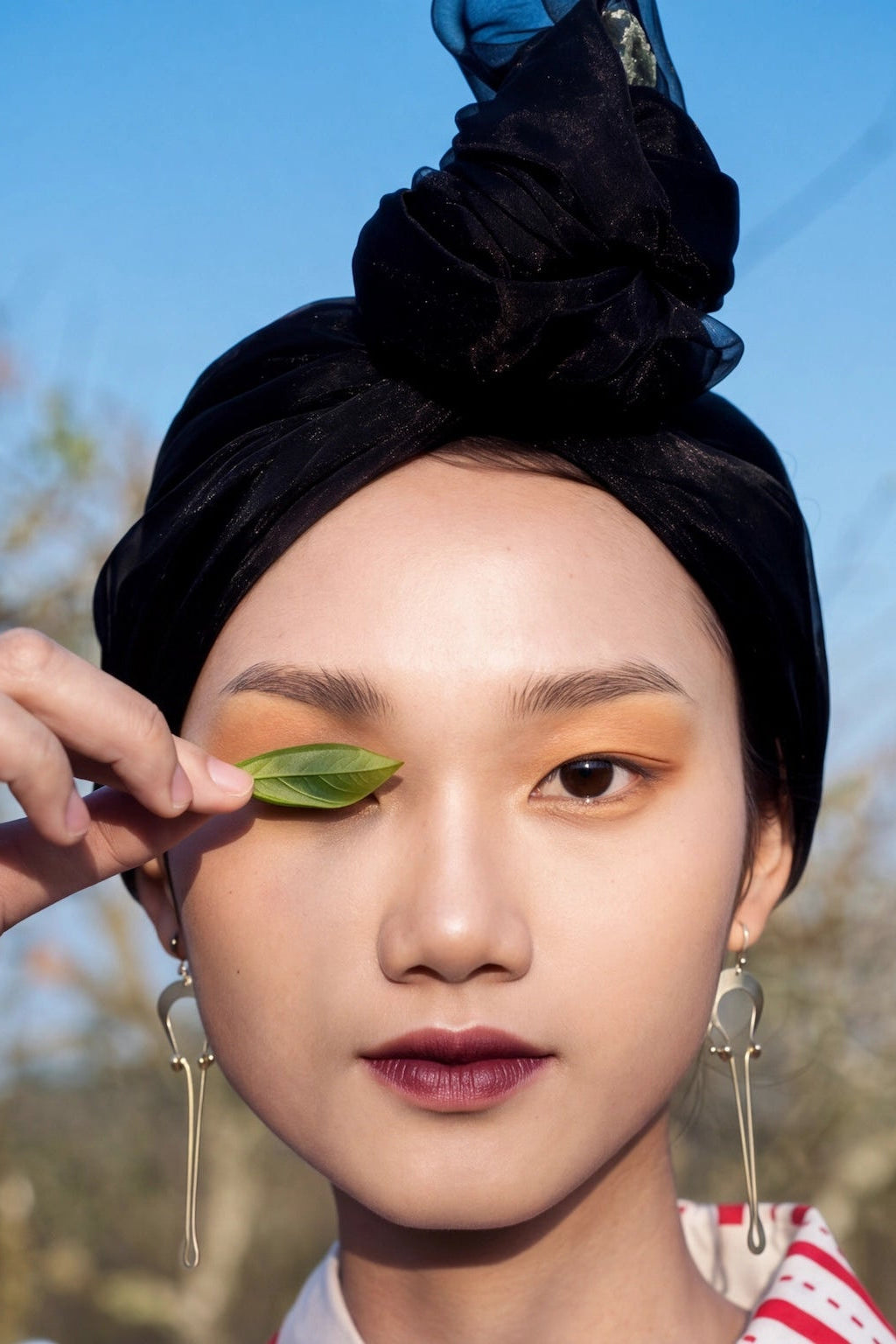 Portrait of a model in a sculpted black turban holding a leaf to her eye