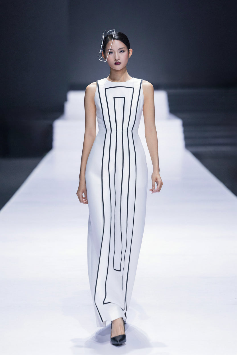 Model on the runway in a white column dress drawn with fine black lines