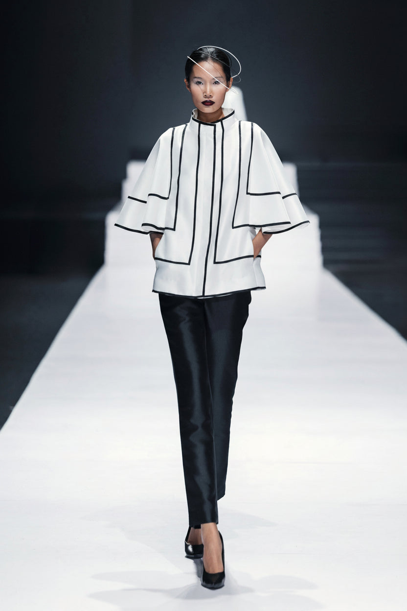 Model on the runway in a white jacket outlined in black