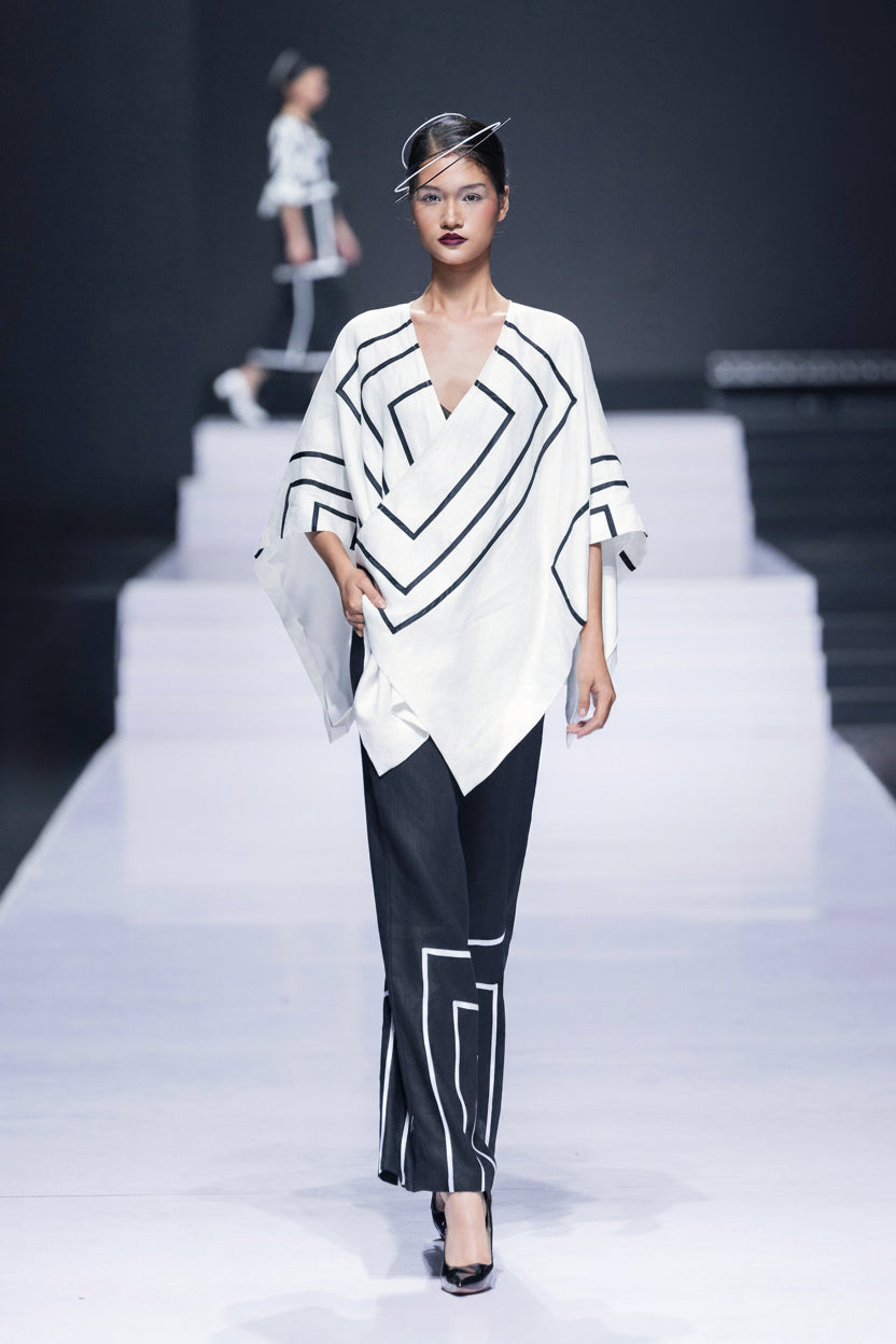 Model on the runway in a white asymmetric jacket drawn with black lines