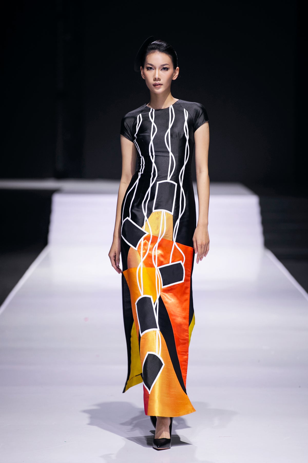 Model on the runway in a black gown painted with orange film frames