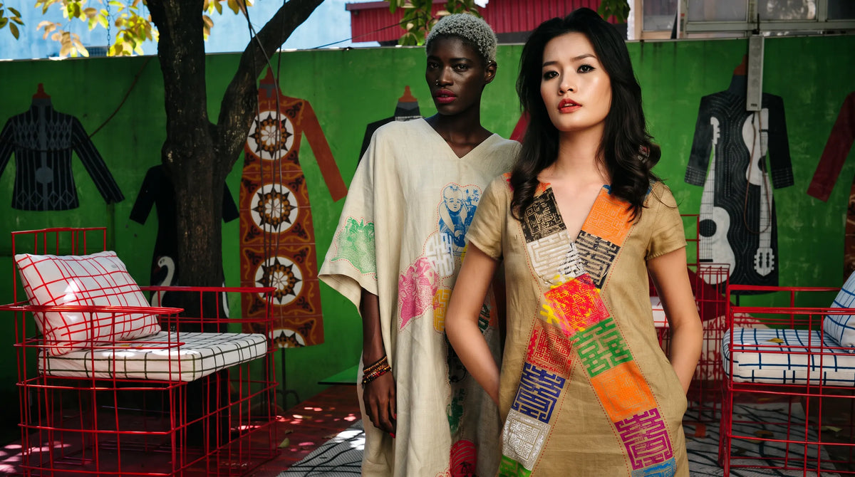 Two models in hand-painted patchwork kaftans in a room hung with rugs and guitars