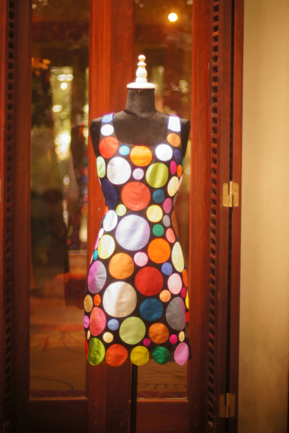 A dress appliqued with bright circles on a stand in a lit doorway, from the Circles collection of 2006