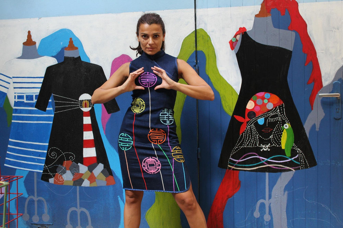 A woman in a navy Chula dress standing before a painted wall of dresses in the Hanoi showroom