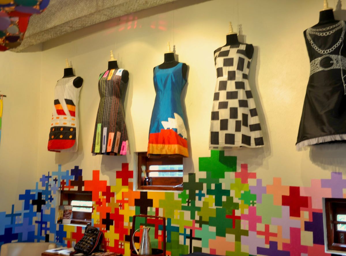 Hand-painted dresses on mannequins against a wall of coloured crosses